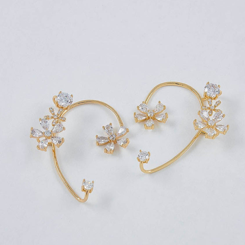 Pair of gold earrings with floral designs on a light gray background
