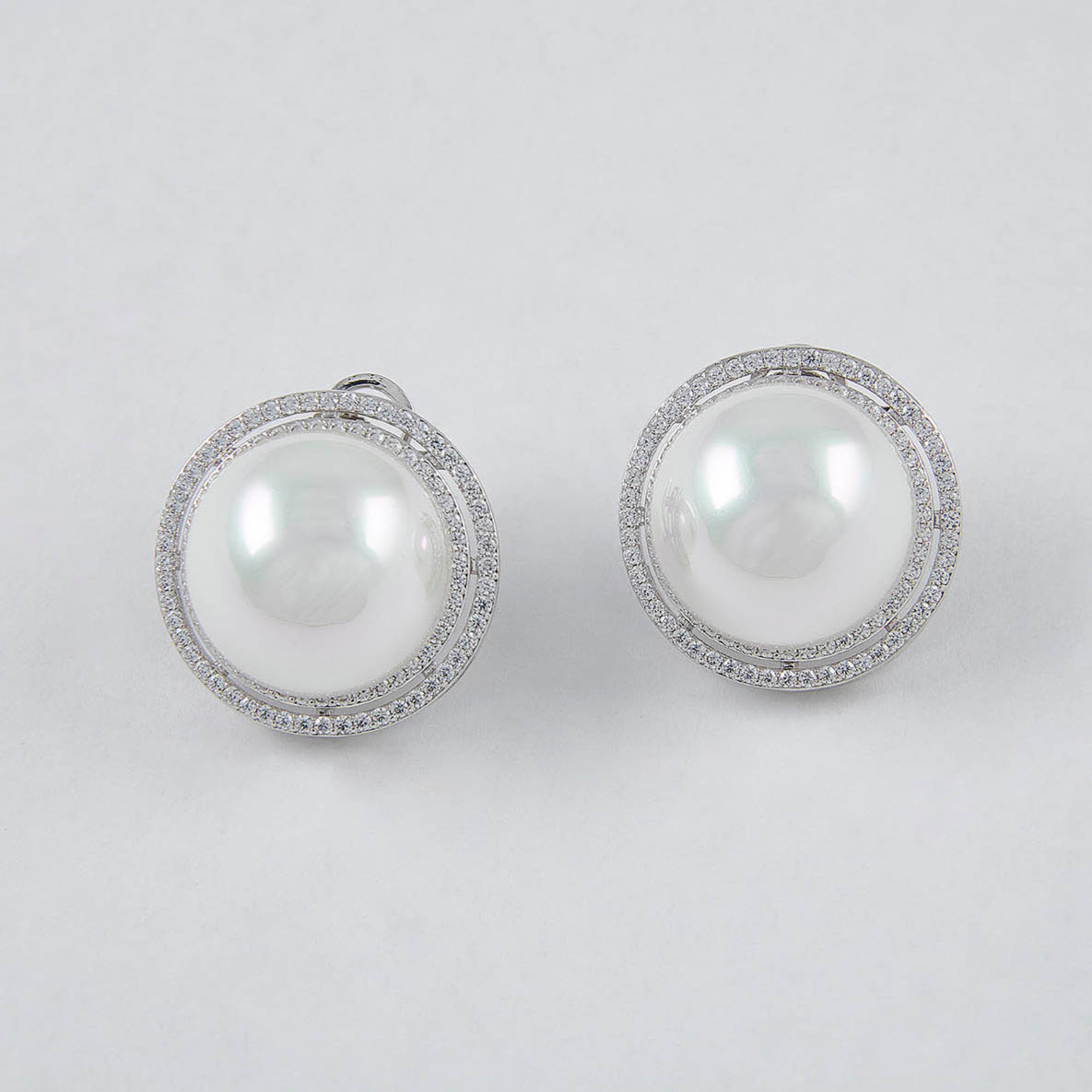 Pair of pearl earrings with silver frames on a light gray background