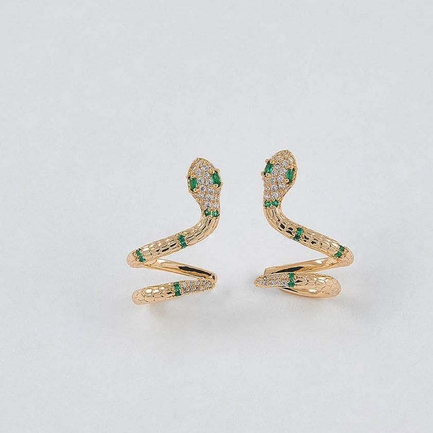 Gold snake-shaped earrings with green gemstones on a light gray background